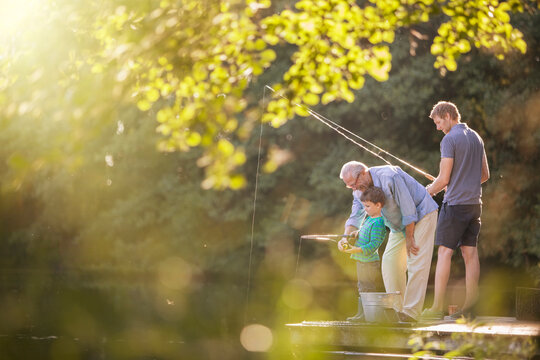 Grandfather, father, and son fishing together from a sunny lake dock